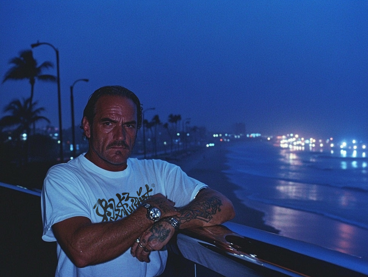 Man with tattoos leaning against a railing by a beach at night
